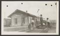 Photograph: [Men standing on train tracks next to a building]