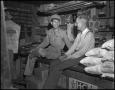 Photograph: [Two men sitting on a store counter]