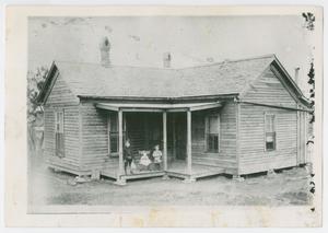 [Photograph of three children on the porch of a wooden house]