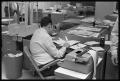 Photograph: [Man Sitting at Desk in Newsroom]