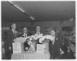 Photograph: [Four men wearing suits, standing behind a display for National Flowe…