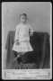 Photograph: [A young man dressed in a white shirt with white ruffled skirt.]