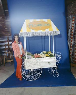 Primary view of [Lynda Arnold posing next to a studio flower stand, 2]