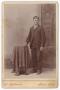 Photograph: [Unknown Man Standing Next to Fabric Covered Table]