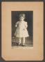 Photograph: [Photograph of a Young Girl Standing Next to a Chair]