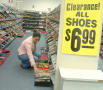 Photograph: [Woman kneeling next to shelves of shoes]