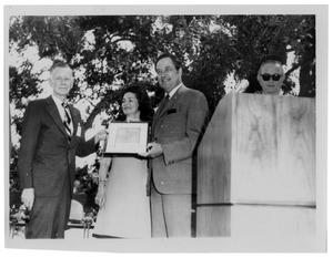 [Two Men Hold a Framed Certificate in Front of Lady Bird Johnson]