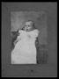 Photograph: [An infant sitting in a chair and wearing a white gown with lace inse…