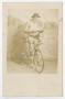 Photograph: [Photograph of Man Standing Against Backdrop with Bicycle]